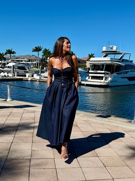 Woman in a navy blue dress standing on a dock with boats in the background