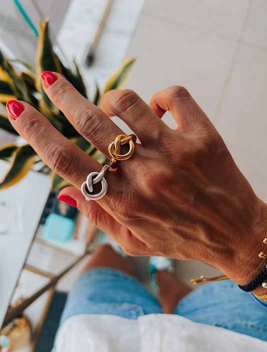 Hand wearing a gold and silver ring with a blurred indoor background