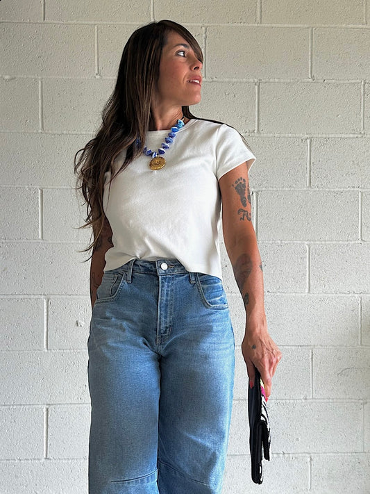 Woman wearing a white t-shirt and blue jeans against a light brick wall.