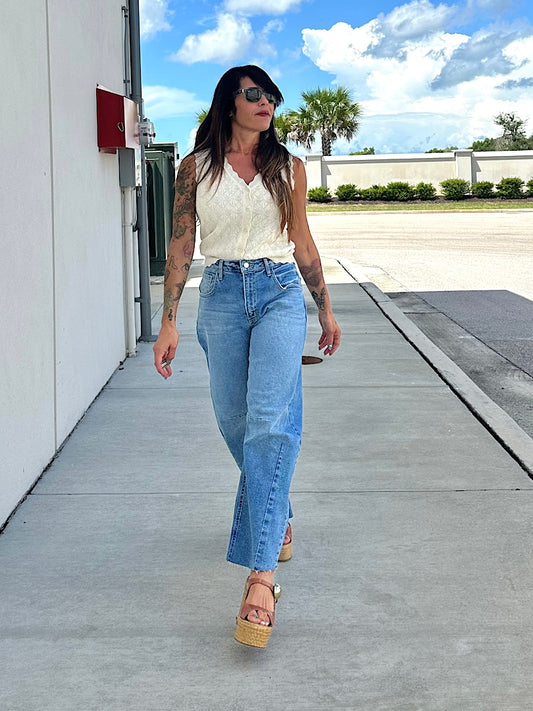 Woman walking on a sidewalk wearing a white top and blue jeans.