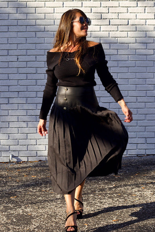 Woman in a black outfit walking against a light gray brick wall.