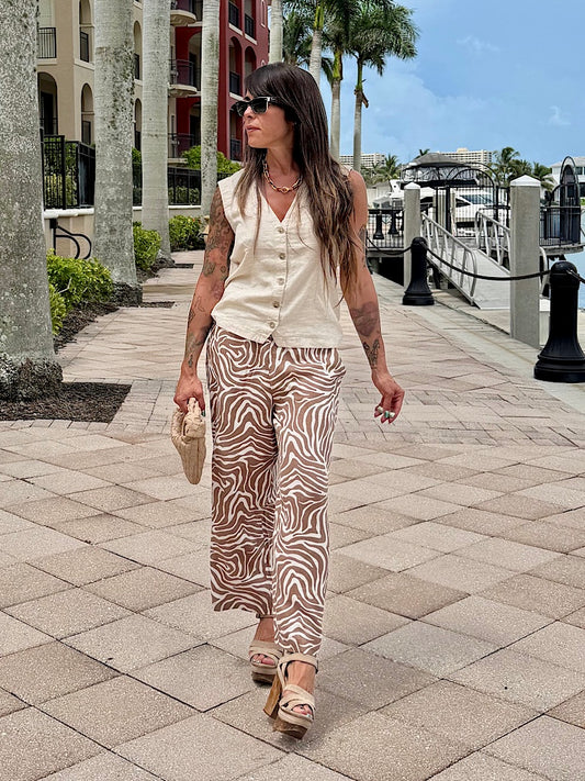 Woman walking on a sidewalk near a waterfront with palm trees and buildings in the background.