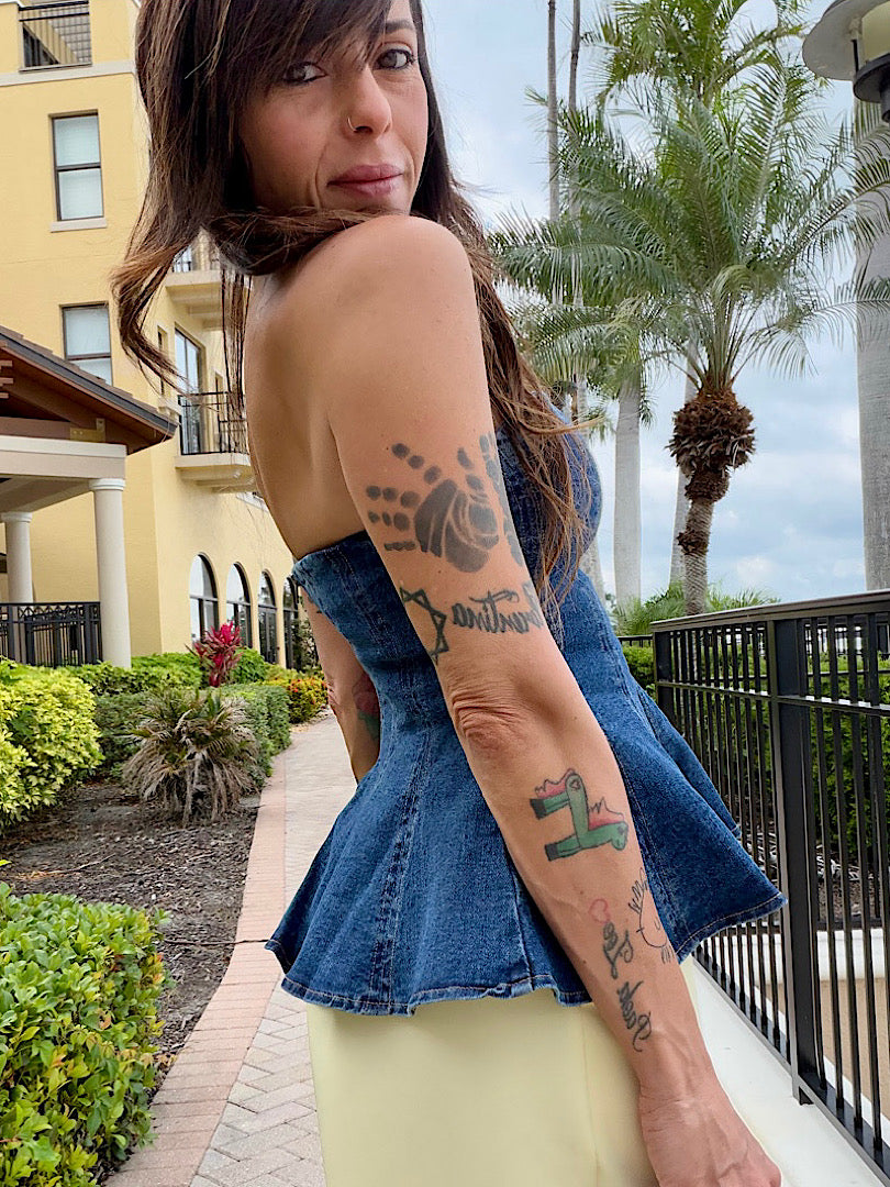 Woman with tattoos on her arms standing outdoors with palm trees and a building in the background