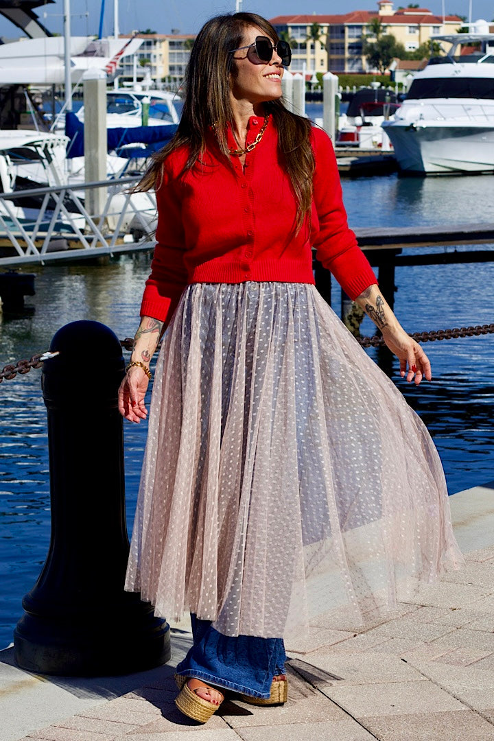 Woman in a red top and long beige skirt standing by a marina.