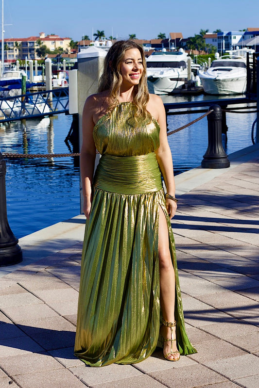 Woman in a metallic gold evening gown standing by a marina with boats in the background.