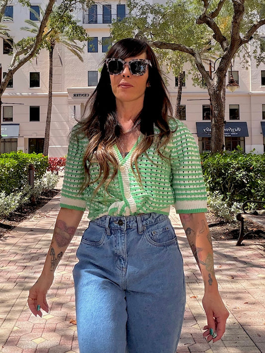 Woman wearing a green knitted top and blue jeans walking outdoors.