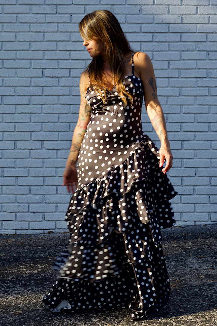 Woman wearing a black and white polka dot dress against a light blue brick wall.