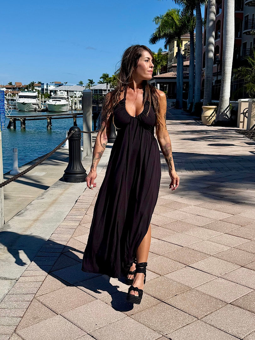 Woman in a black dress standing on a dock with water and palm trees in the background