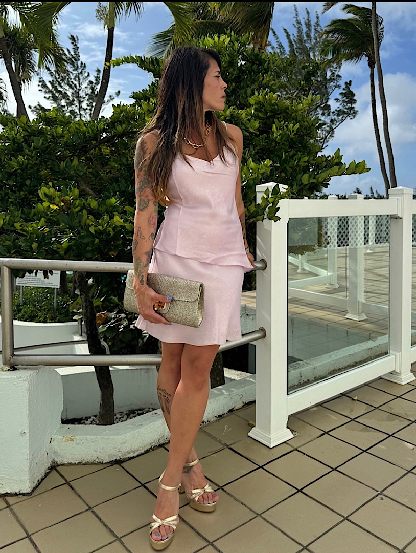 Woman in a pink dress standing on a tiled patio with greenery in the background