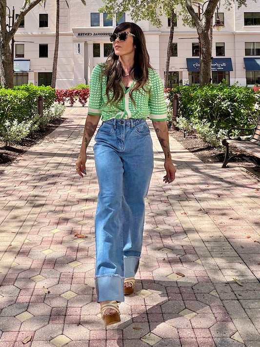 Woman walking on a sidewalk wearing a green patterned shirt and blue jeans.