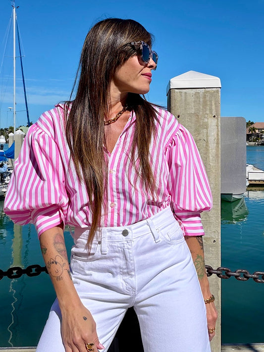 Woman in a pink and white striped shirt and white pants standing by a marina.