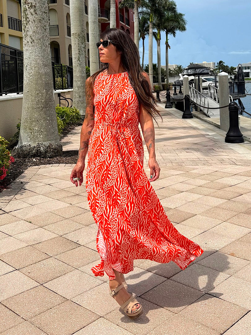 Woman in an orange patterned dress walking along a waterfront promenade.