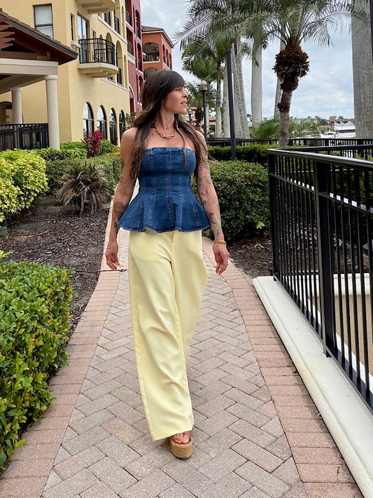 Woman walking on a sidewalk wearing a blue peplum top and yellow pants.