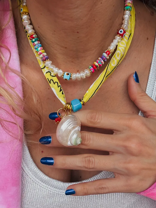 Colorful beaded necklace with a shell pendant worn by a person with blue nail polish.