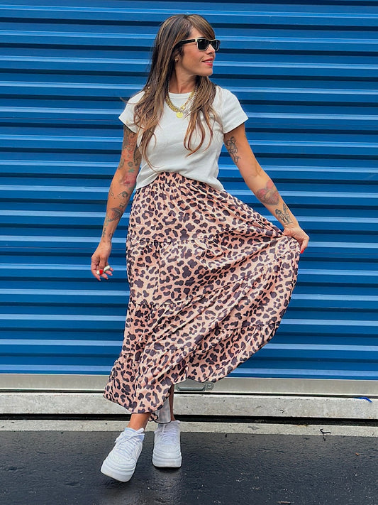 Woman wearing a white t-shirt and leopard print skirt against a blue corrugated metal background