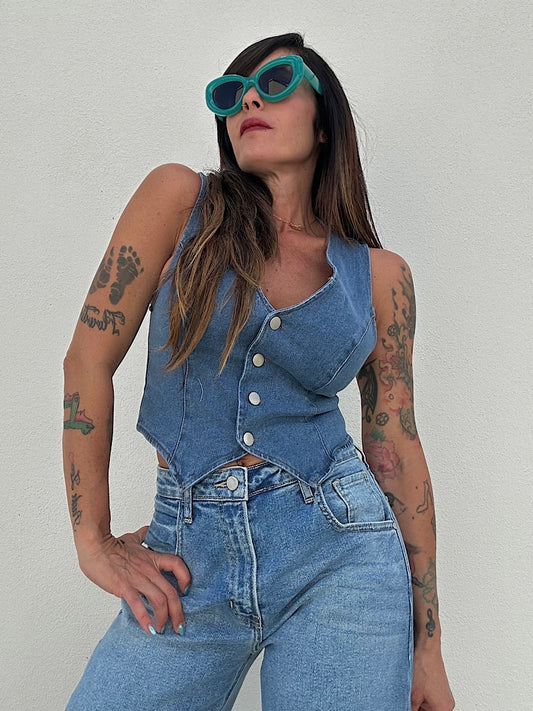 Woman wearing a denim vest and jeans with tattoos on a plain background